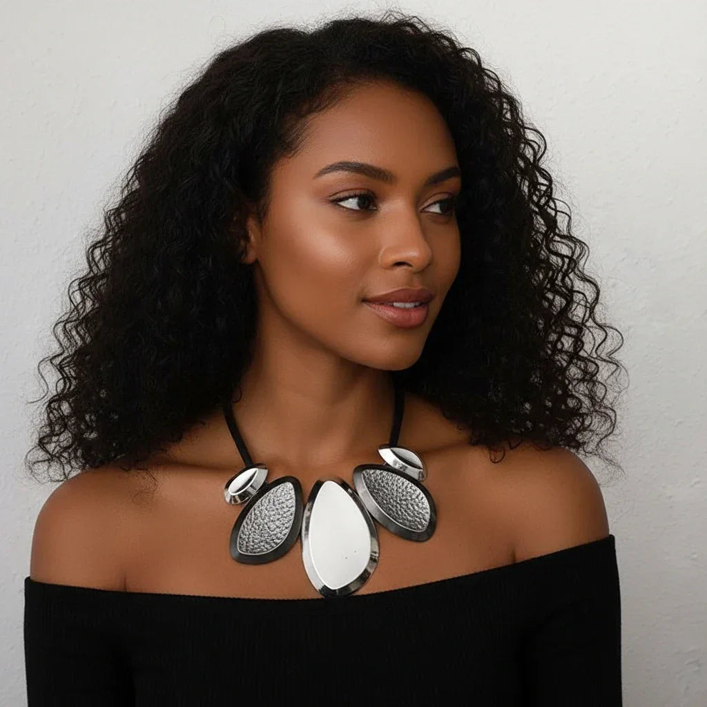 Woman wearing a black off-shoulder top and a large, silver, layered necklace against a neutral background.