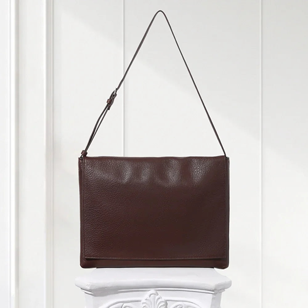 Minimalist dark brown lambskin messenger bag with front flap, adjustable shoulder strap, and slim rectangular design for women.