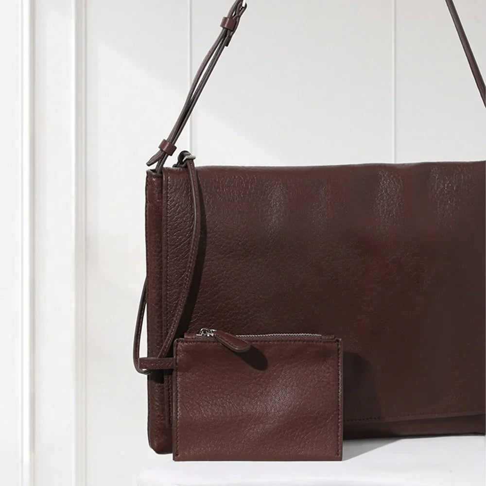 Minimalist dark brown lambskin messenger bag with front flap, adjustable shoulder strap, and slim rectangular design for women.