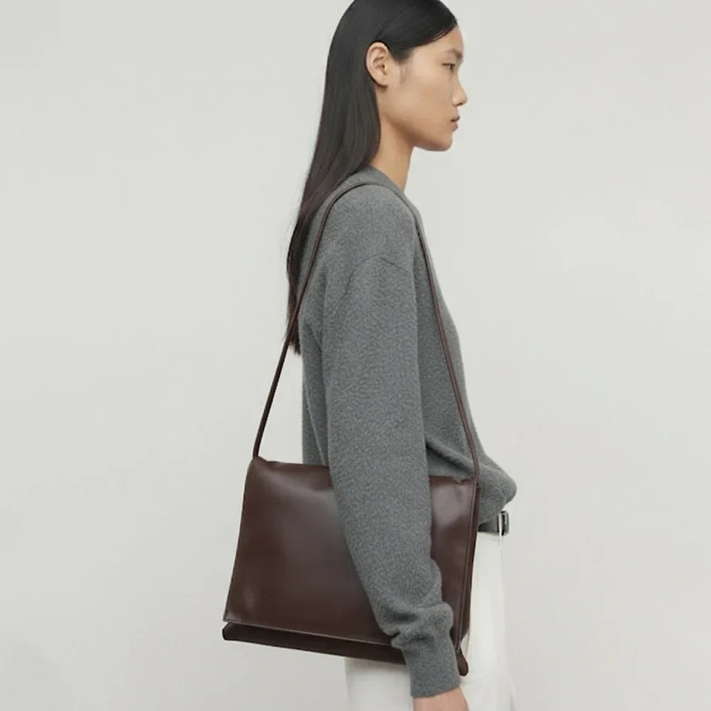 Minimalist dark brown lambskin messenger bag with front flap, adjustable shoulder strap, and slim rectangular design for women.