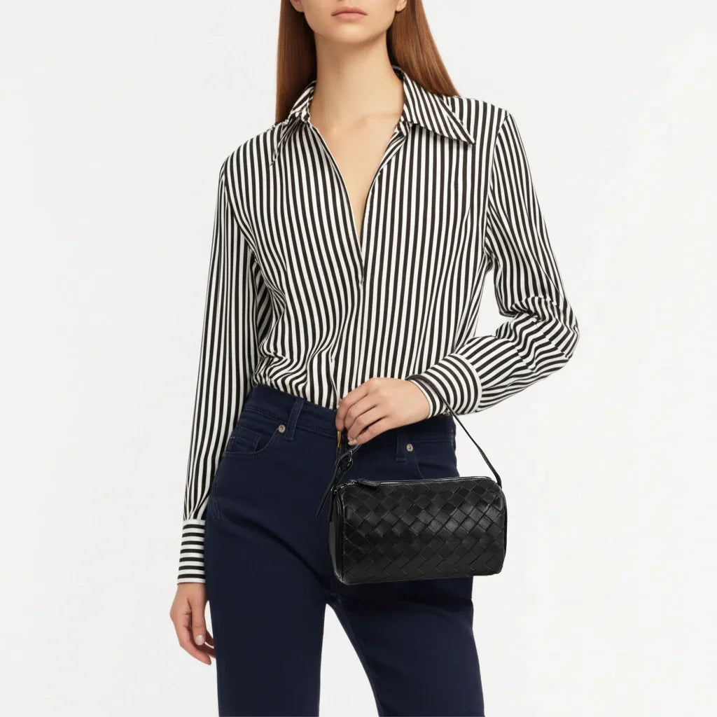 Woman holding a black woven leather handbag, stylish shoulder bag for everyday and evening wear.