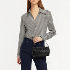 Woman holding a black woven leather handbag, stylish shoulder bag for everyday and evening wear.