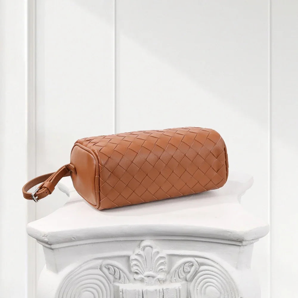 Brown woven handbag on a decorative white pedestal against a light gray background