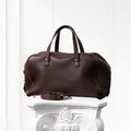 Brown leather duffel bag on a decorative white pedestal against a light gray background