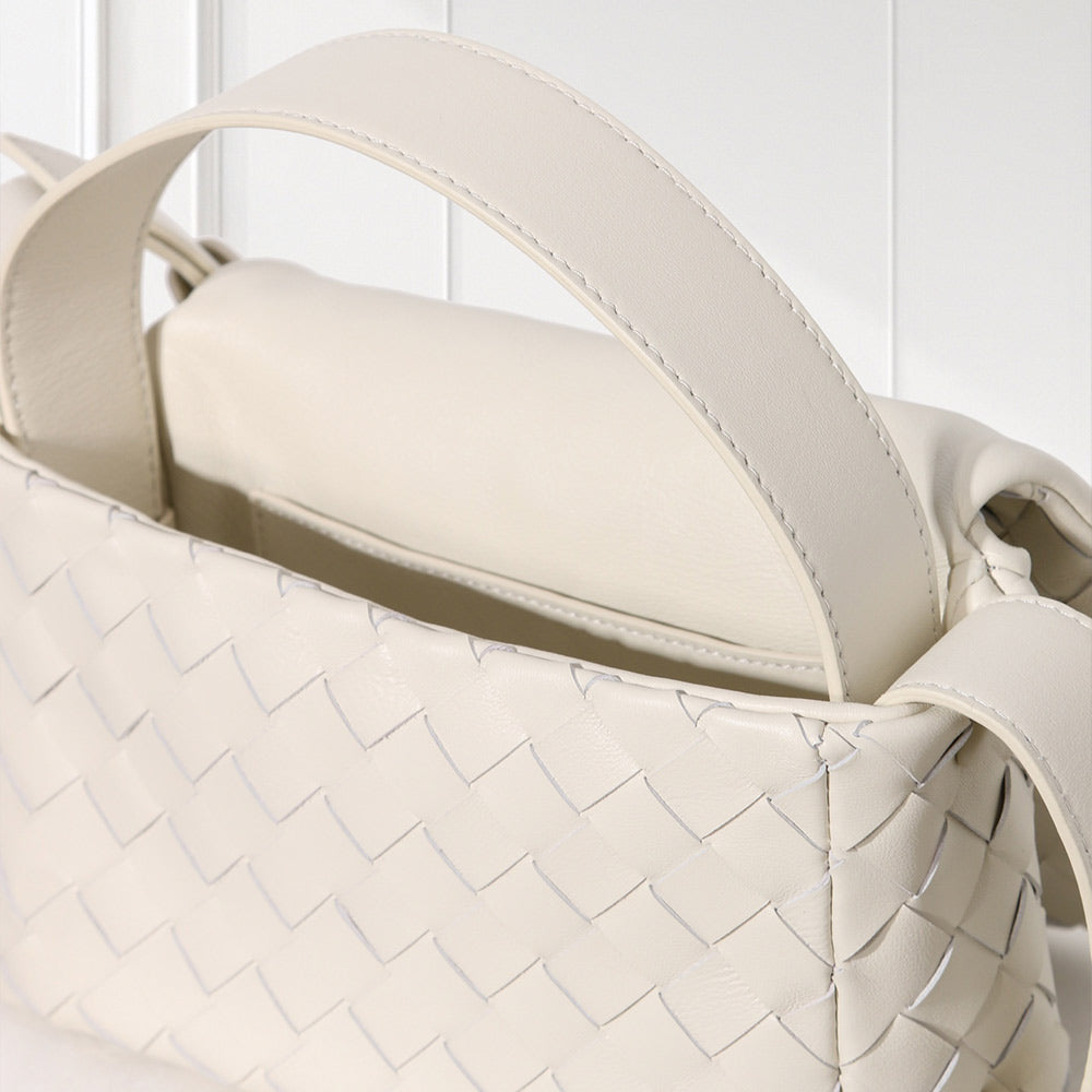 A close-up of a woven leather handbag in a warm off-white or cream color, showing the detailed basketweave texture and the top handle against a light background.