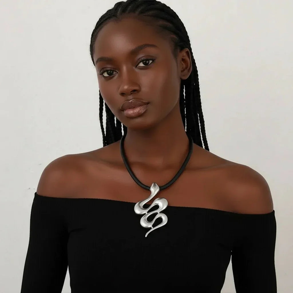 Woman wearing a black off-shoulder top and a silver snake pendant necklace against a plain background