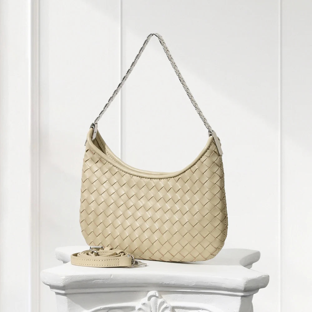 Beige woven handbag on a white pedestal against a white background