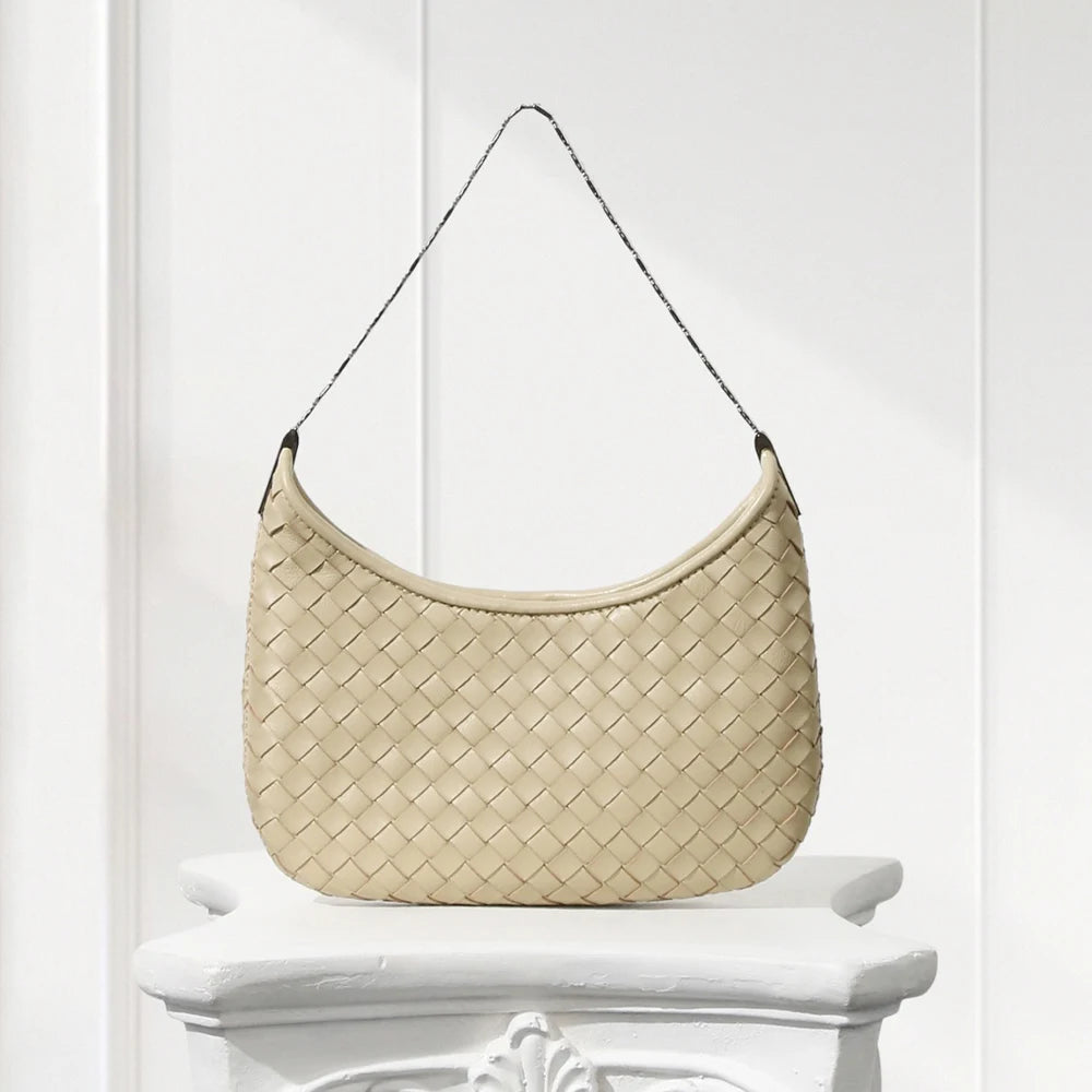Beige woven handbag on a white pedestal against a white background
