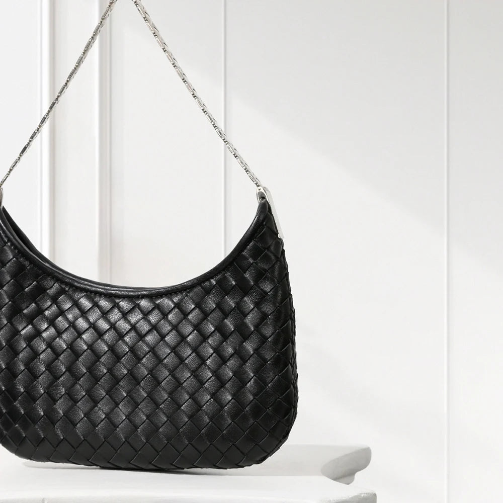 Black woven handbag on a white surface with a white background