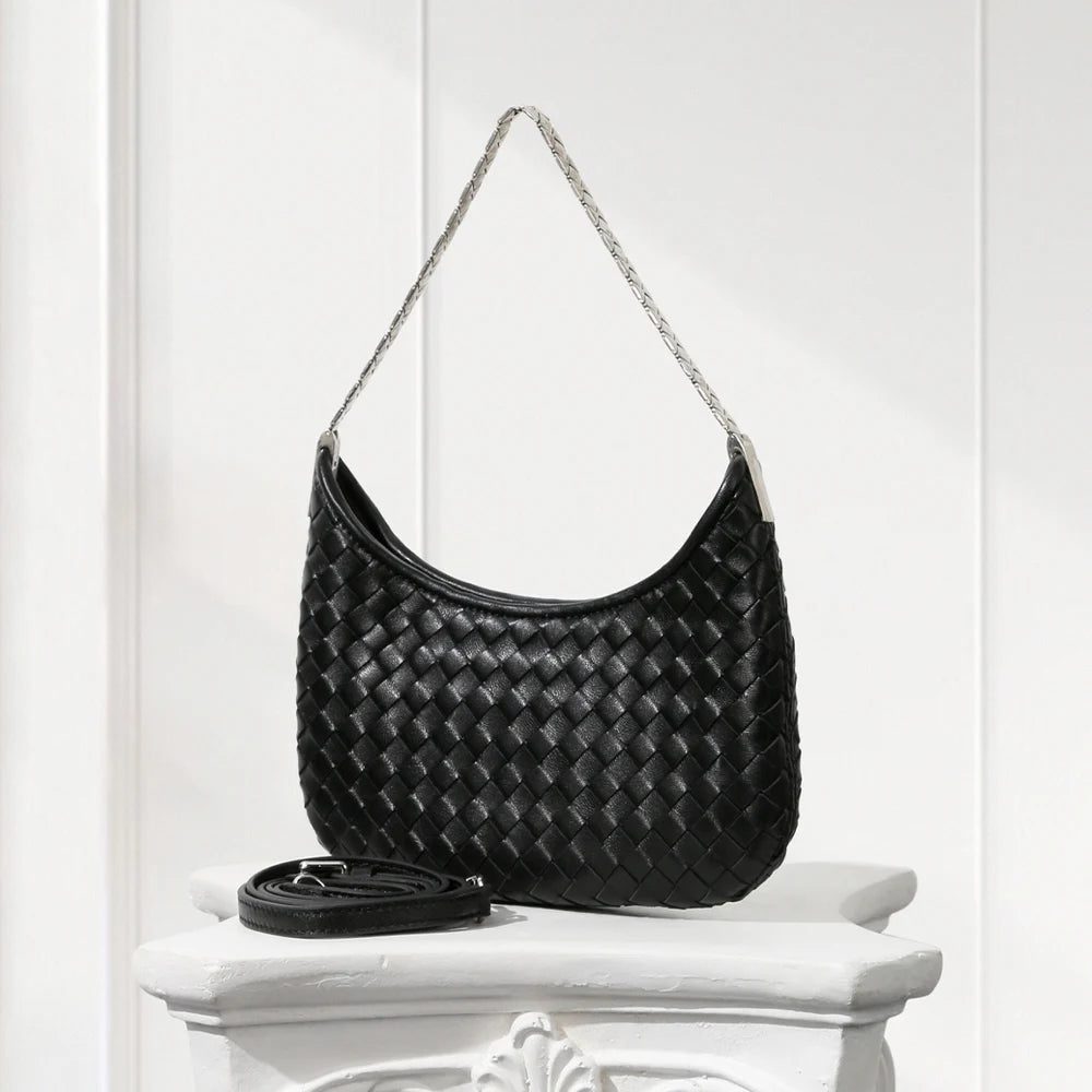 Black woven handbag on a white pedestal against a white background