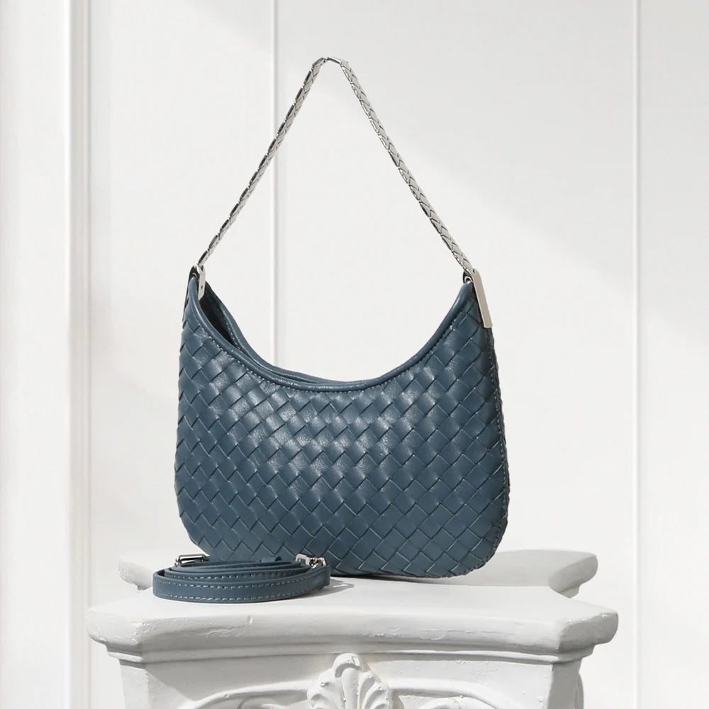 Blue woven handbag on a white pedestal against a white background