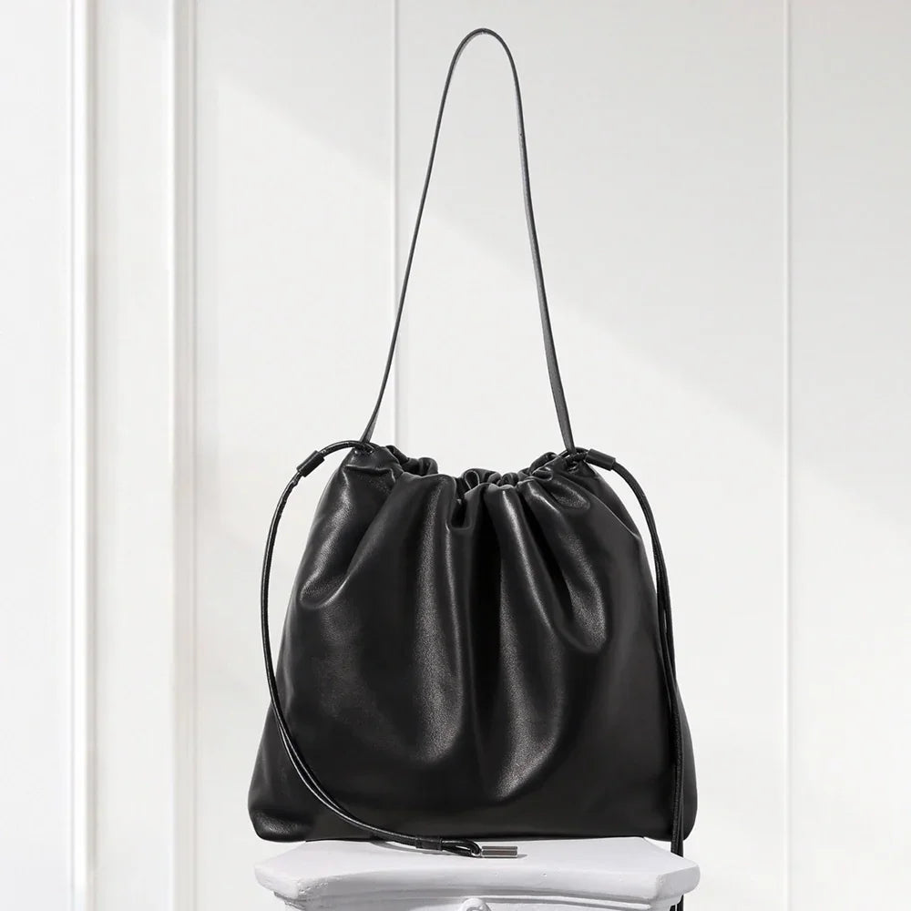 Black leather drawstring bag on a white surface with a white curtain background