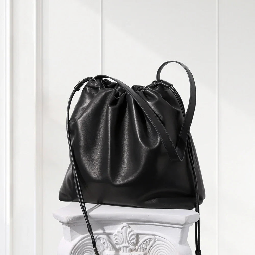 Black leather drawstring bag on a decorative white pedestal against a light wooden panel background