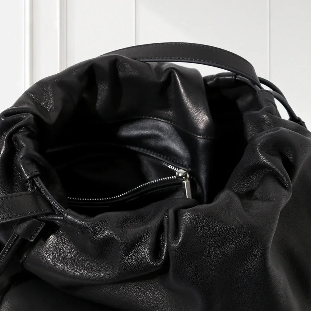 Close-up of a black leather drawstring bag with a zipper on a white background