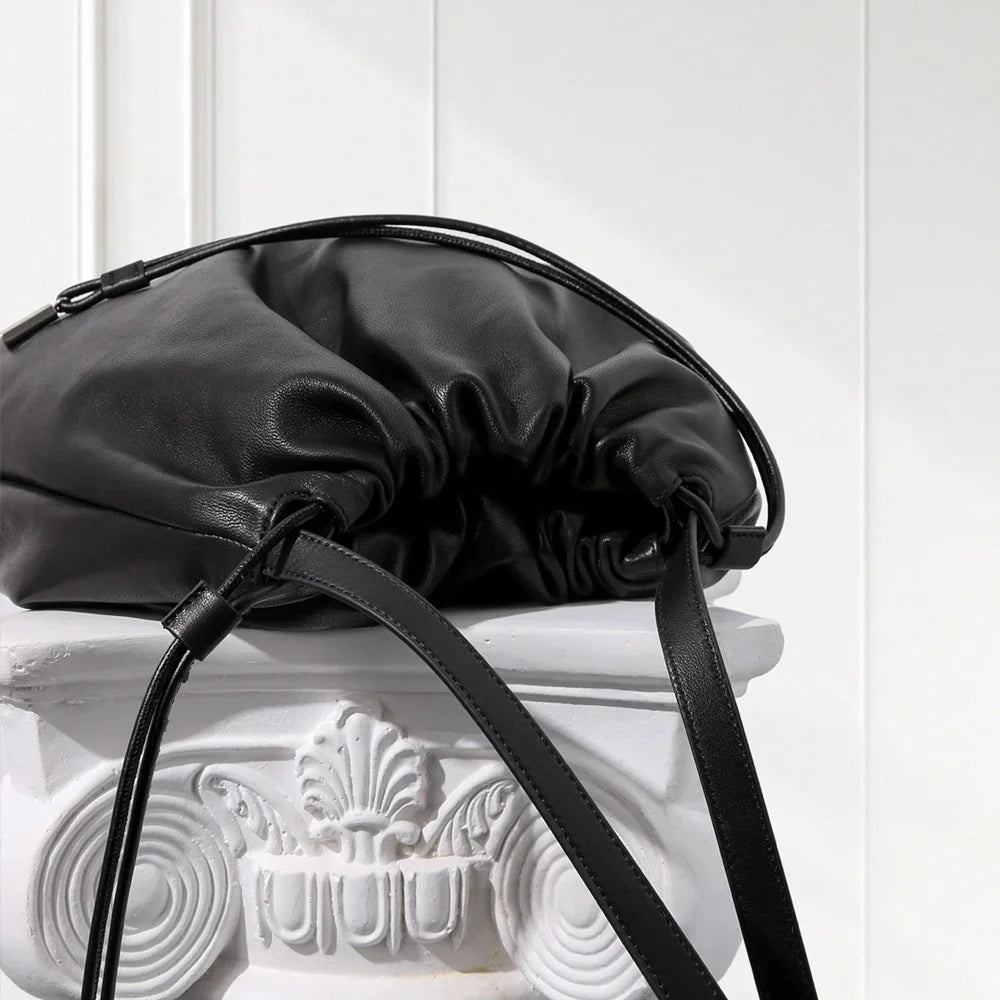 Black leather handbag with a strap on a decorative white pedestal