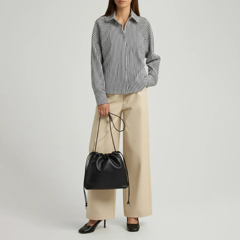 Person wearing a black and white striped shirt and beige pants, holding a black handbag on a light gray background