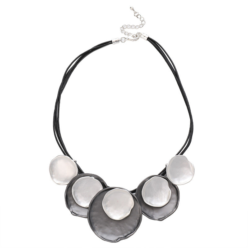A statement necklace featuring five organic-shaped, textured silver discs layered over a multi-strand black cord, with a silver chain clasp at the top, shown on a plain white background.