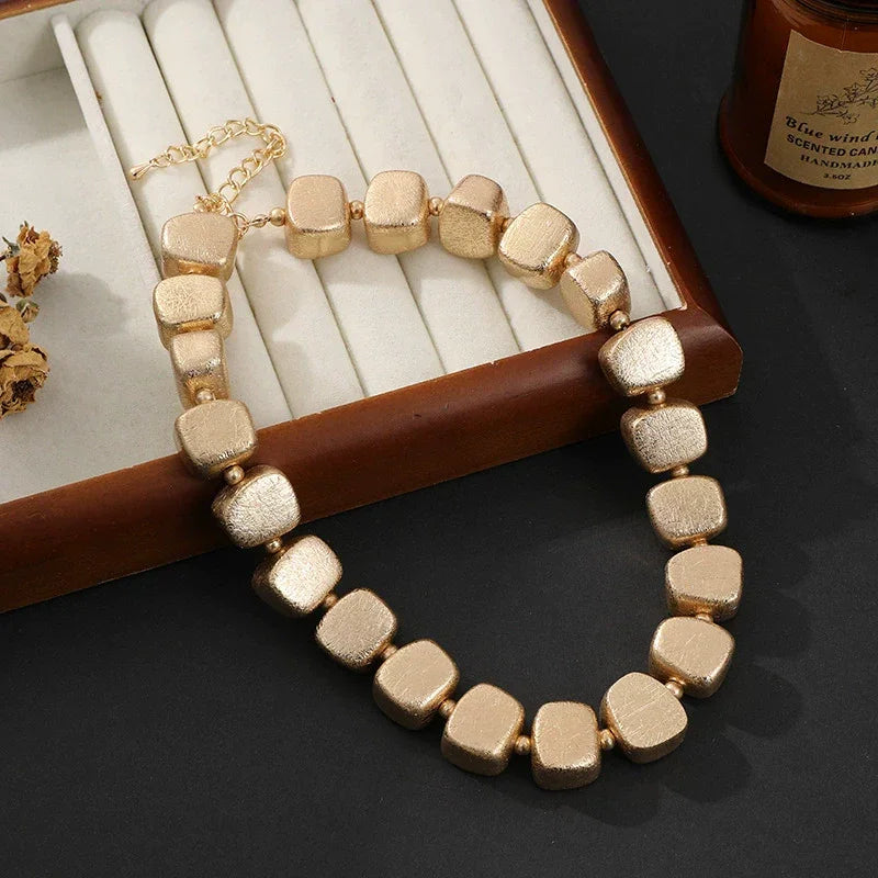 Gold beaded necklace on a dark surface with a jewelry box in the background