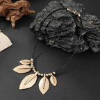 Gold leaf necklace on a dark surface with rocks and driftwood