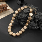 Gold beaded necklace on a dark surface with rocks and a book