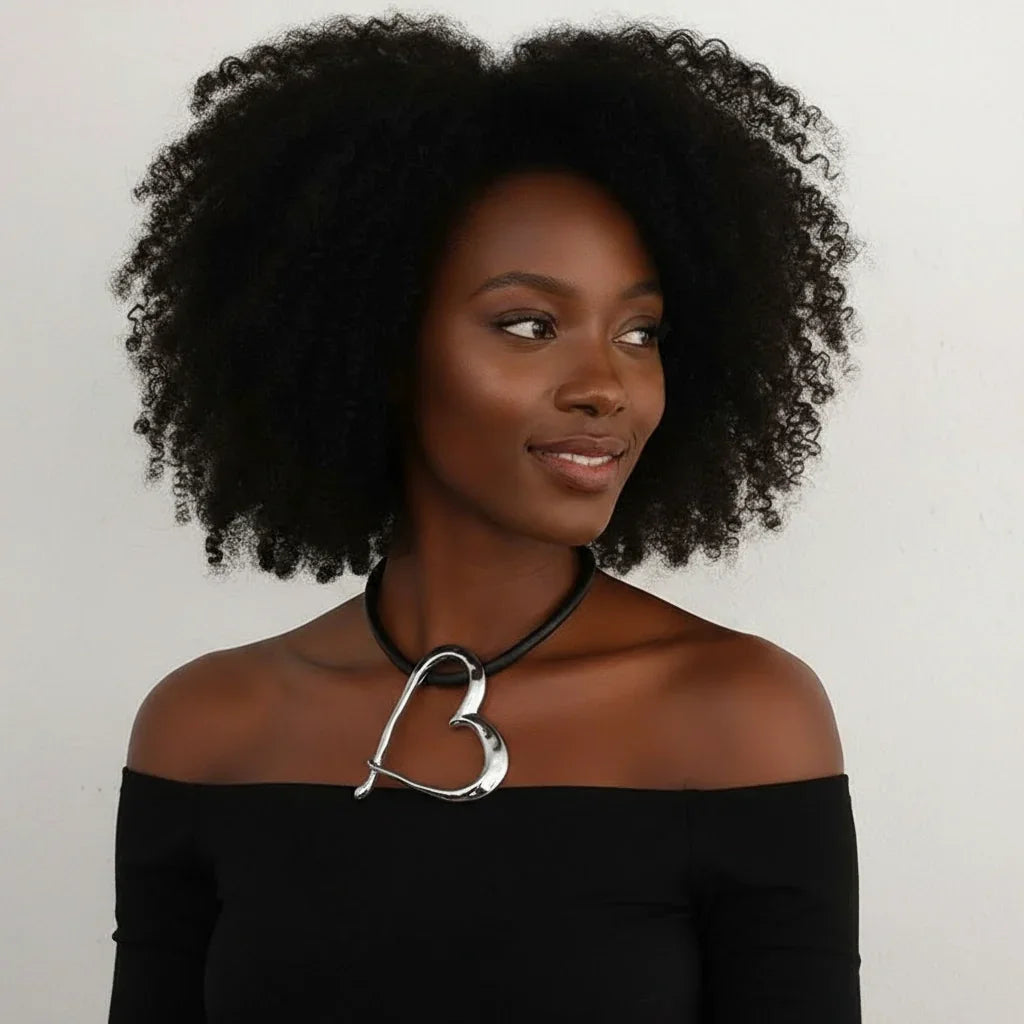 Woman wearing a black off-shoulder top with a necklace featuring a large 'L' pendant on a plain background